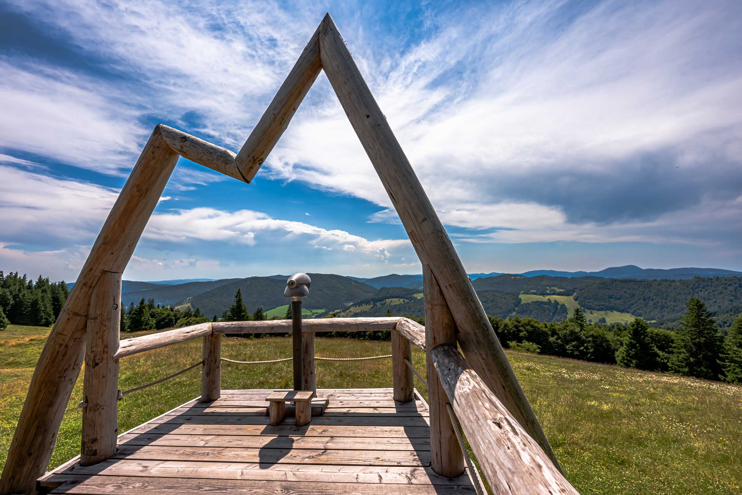 Eine Aussichtsplattform aus Holz mit einem Fernglas und Blick auf die Berge